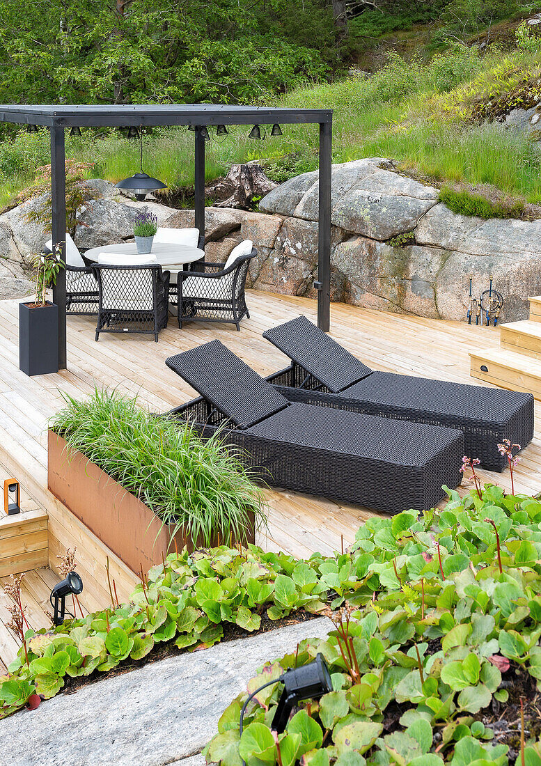 View of wooden terrace with Corten sheet planter box and black rattan loungers