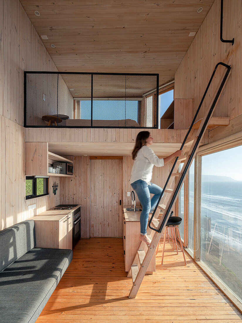 Sleeping area above the kitchen in the wooden house with double room height, woman on ladder