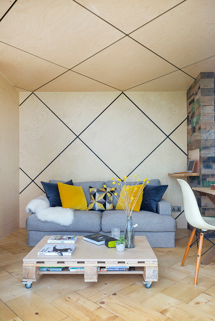 Graues Polstersofa und Palettentisch in offenem Wohnraum, rautenförmige Decke mit LED-Leisten