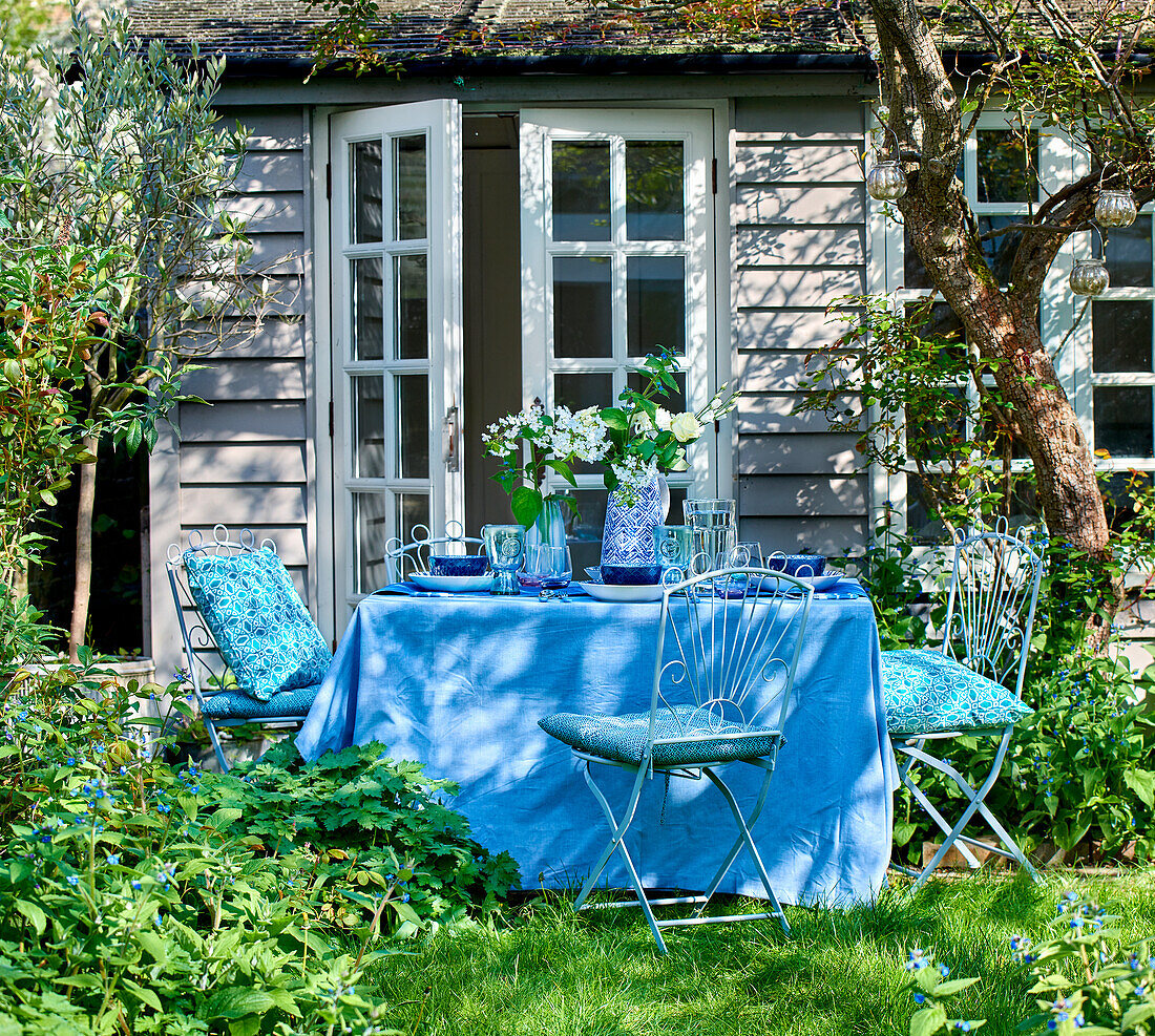 Dining table set in blue in front of summer house