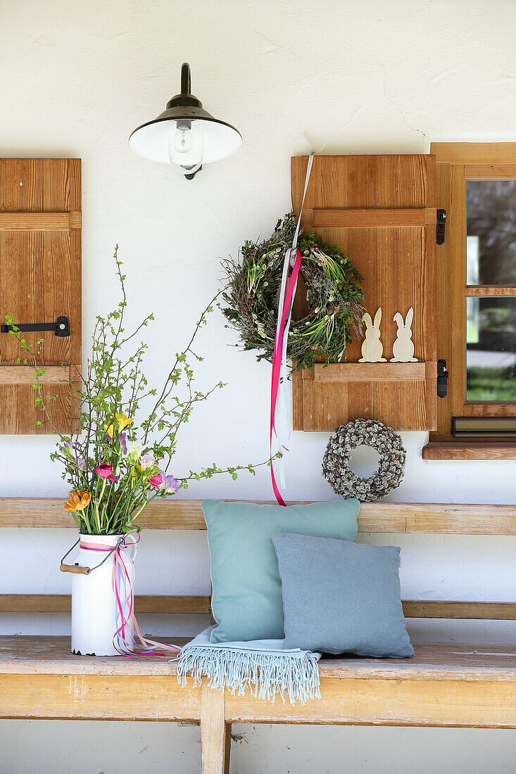 Wooden bench with cushions and spring bouquet under a window shutter decorated for Easter