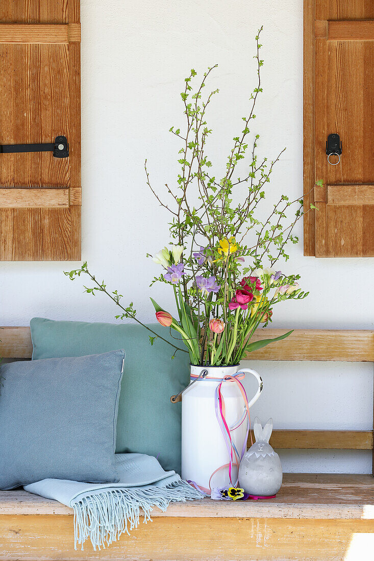Spring bouquet of freesias and tulips (Tulipa) next to cushion on wooden bench