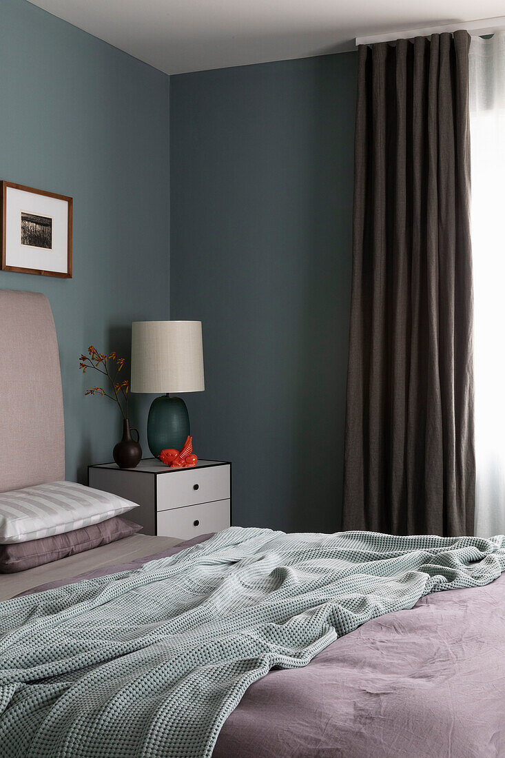 Double bed and bedside table with lamp in bedroom with grey walls
