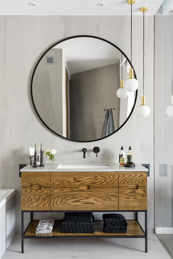 Badezimmer in Hellgrau, großer runder Spiegel, darunter Waschtisch mit Eichenfurnier verkleidet