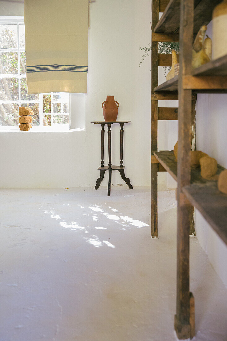 Rustikales Regal, im Hintergrund Beistelltisch mit Tonkrug neben Fenster