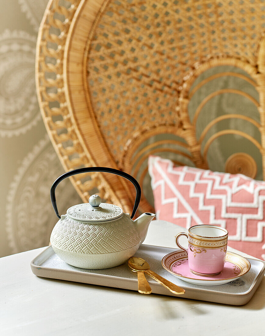 Teekanne und Porzellantasse, im Hintergrund Rattanstuhl