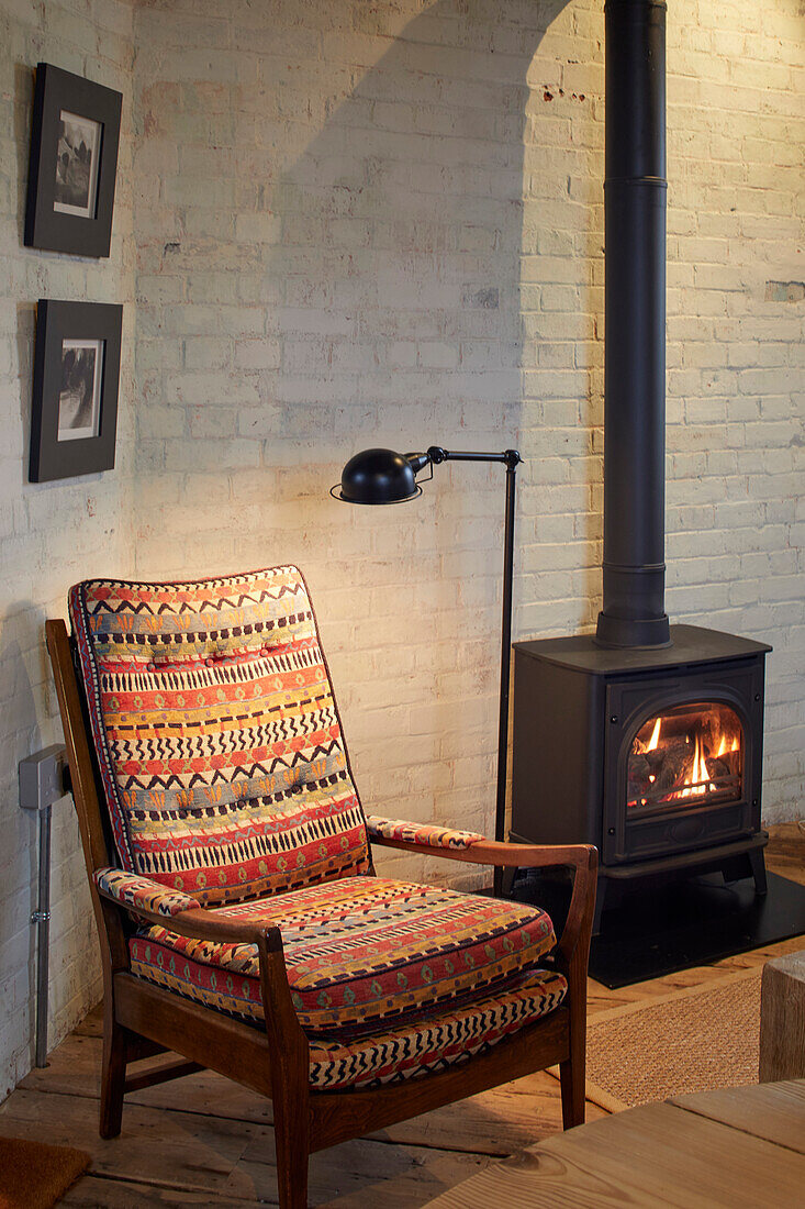 Reading chair next to wood stove in front of rustic brick wall