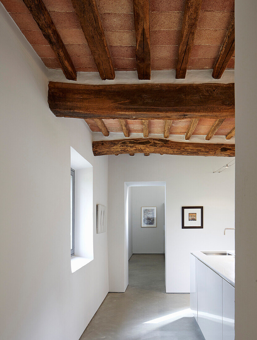 White kitchen with rustic exposed wood ceiling beams in a Tuscan farmhouse, Italy