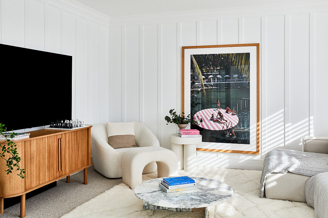 Modern living room with panelled walls, bouclé armchair and footstool and marble coffee table