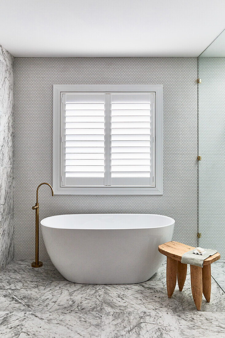 Minimalistisches, weißes Bad mit freistehender Badewanne, goldener Standarmatur, Marmorwand und -boden