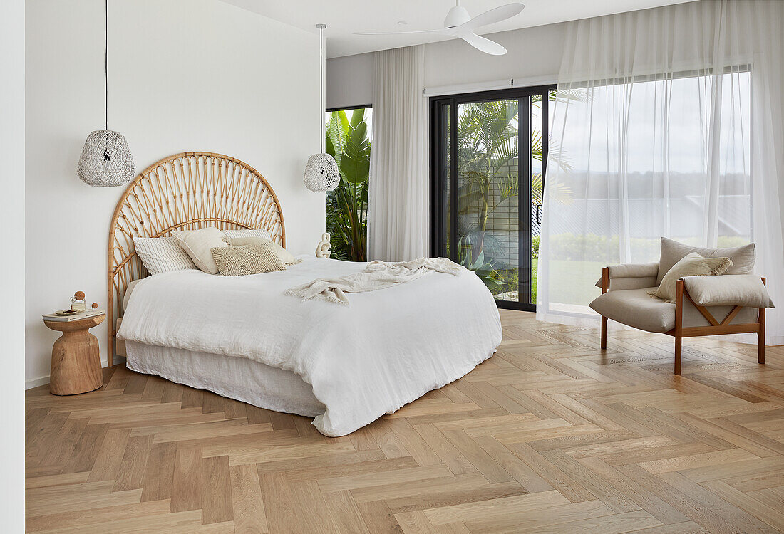 Helles Schlafzimmer mit Betthaupt aus Schilfrohr, Eichenparkett und Blick auf tropischen Garten