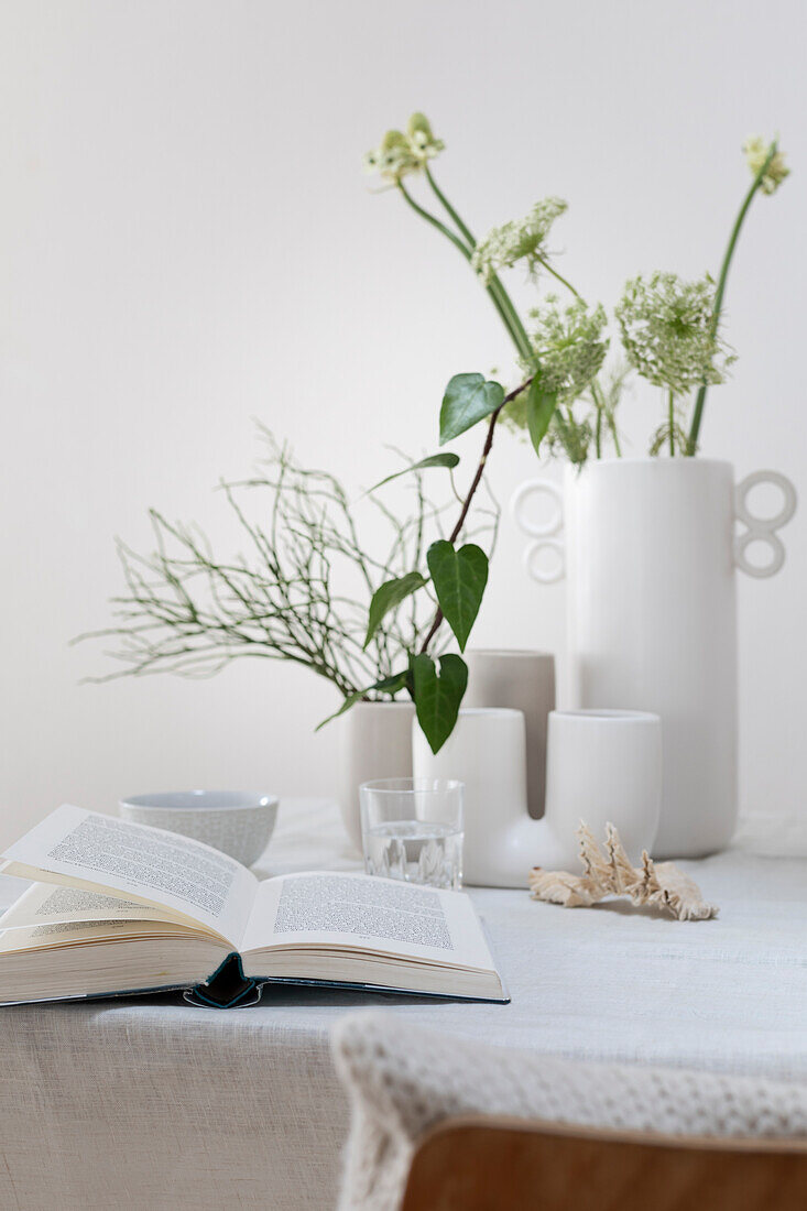 Gedeckter Frühlingstisch mit verschiedenen weißen Vasen, Wilder Möhre, Arabischer Sternblume, Gräser, Efeu und Heidelbeerzweig