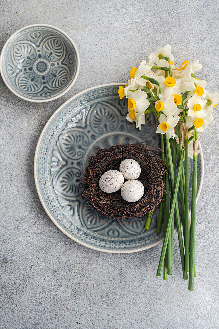 Kleines Osternest mit Eiern und Narzissen (Narcissus) auf Keramikteller