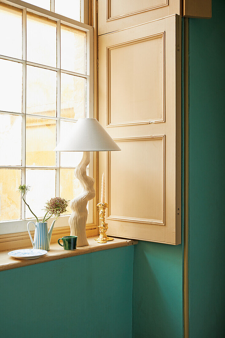 Zimmer mit grüner Wand und Fensterladen, künstlerisch gestaltete Tischlampe auf Fensterbank