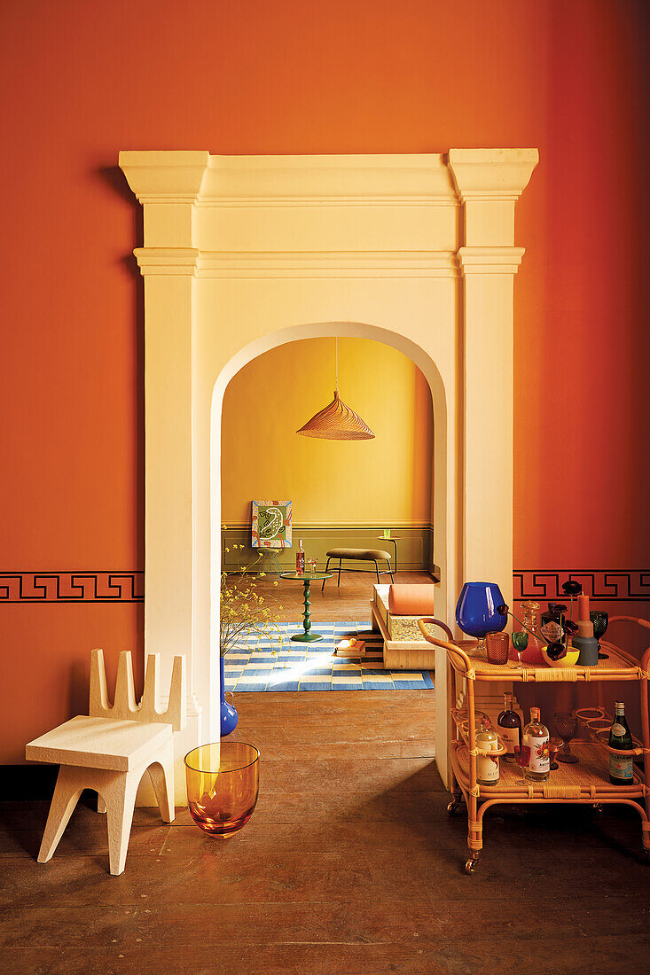 Bar cart and designer stool in front of arched doorway in room with orange wall
