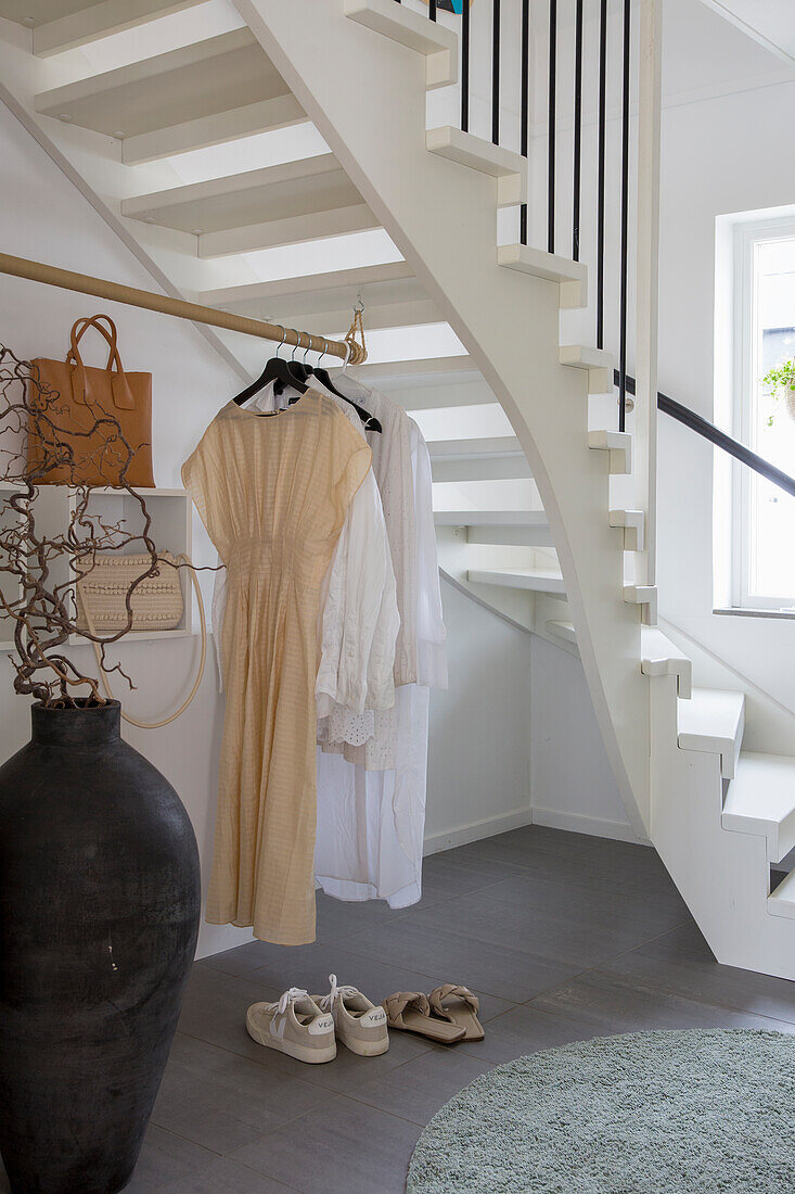 Bright entrance area with white wooden staircase and clothes rack