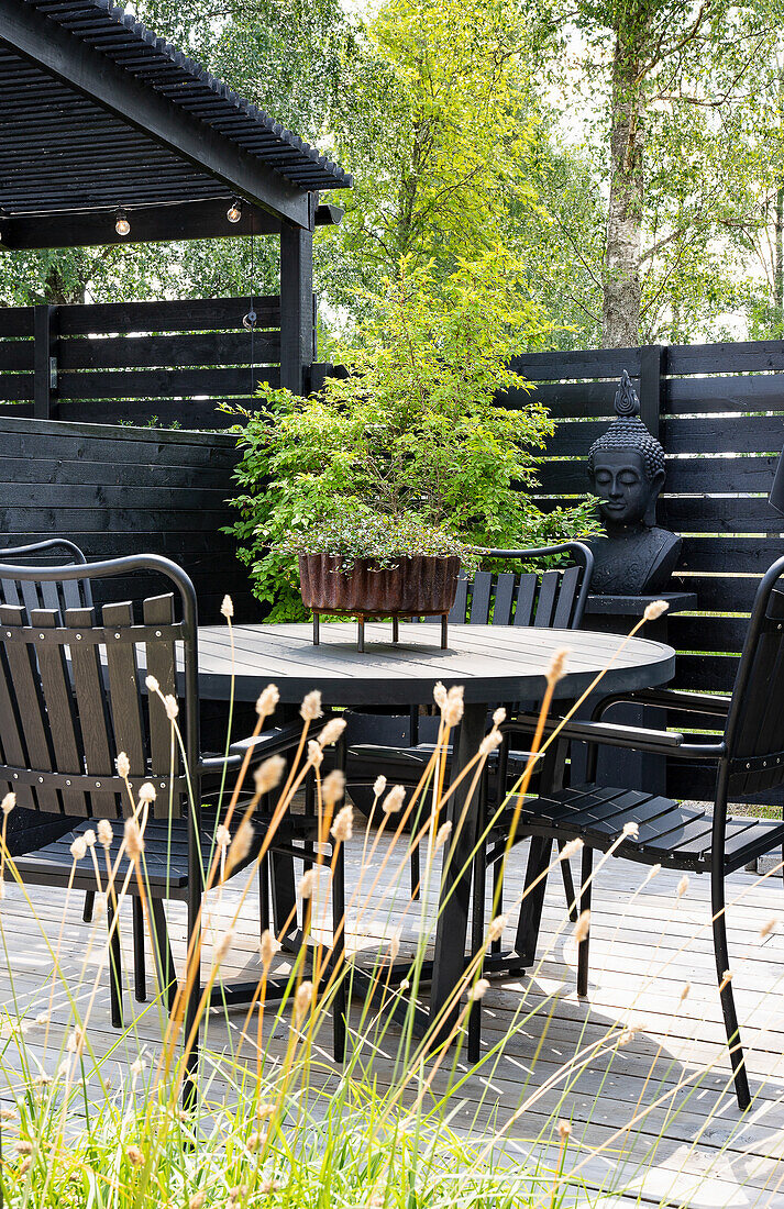 Terrace with table, chairs and Buddha statue in front of black privacy fence