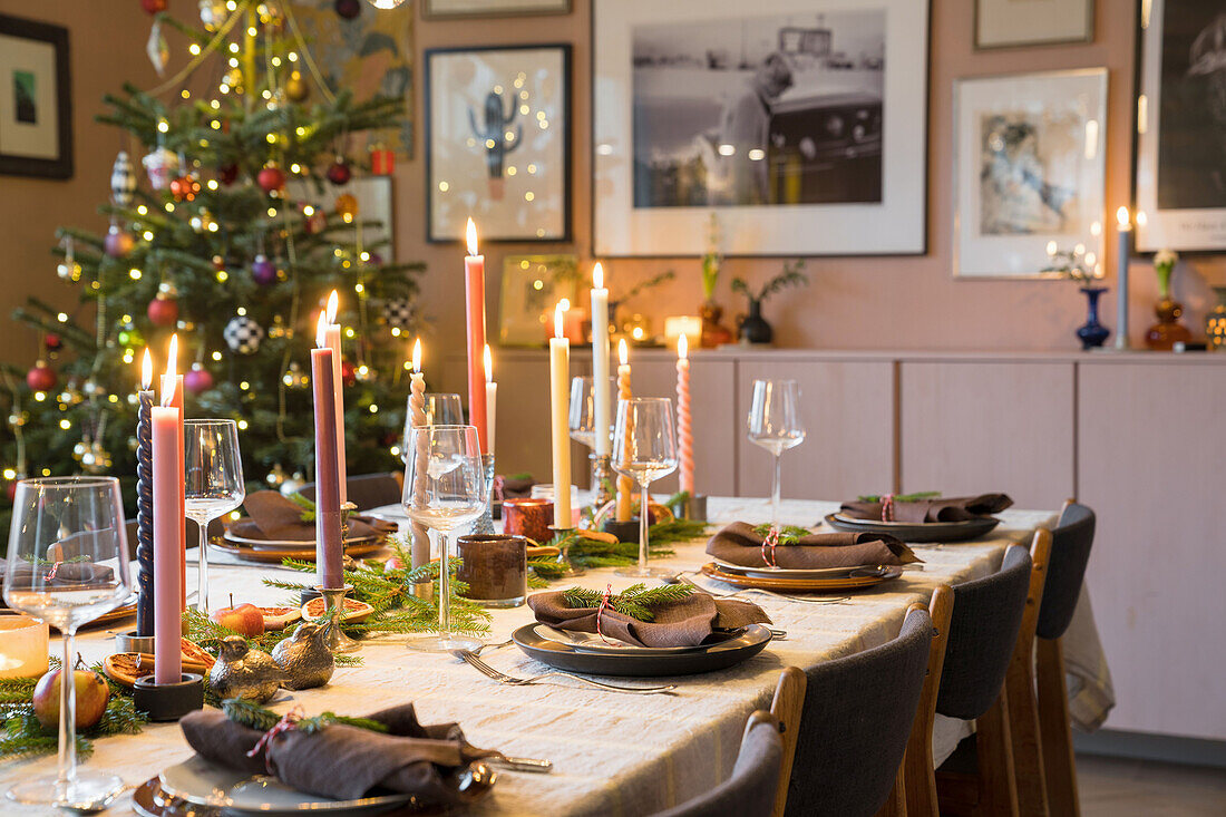 Festlich gedeckter Esstisch mit Kerzen und Weihnachtsbaum im Hintergrund