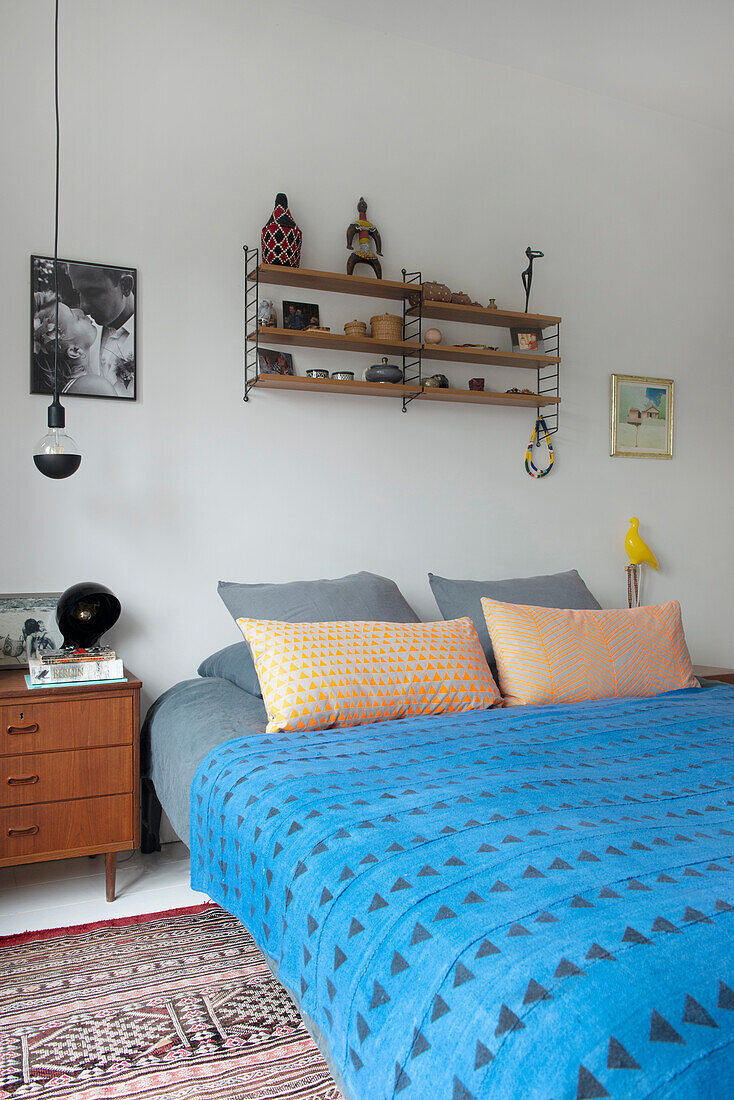 Bed with geometrically patterned bed linen and wall shelf with decorative objects