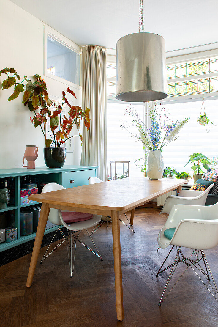 Wooden table and white chairs in bright dining area with plants and pendant light