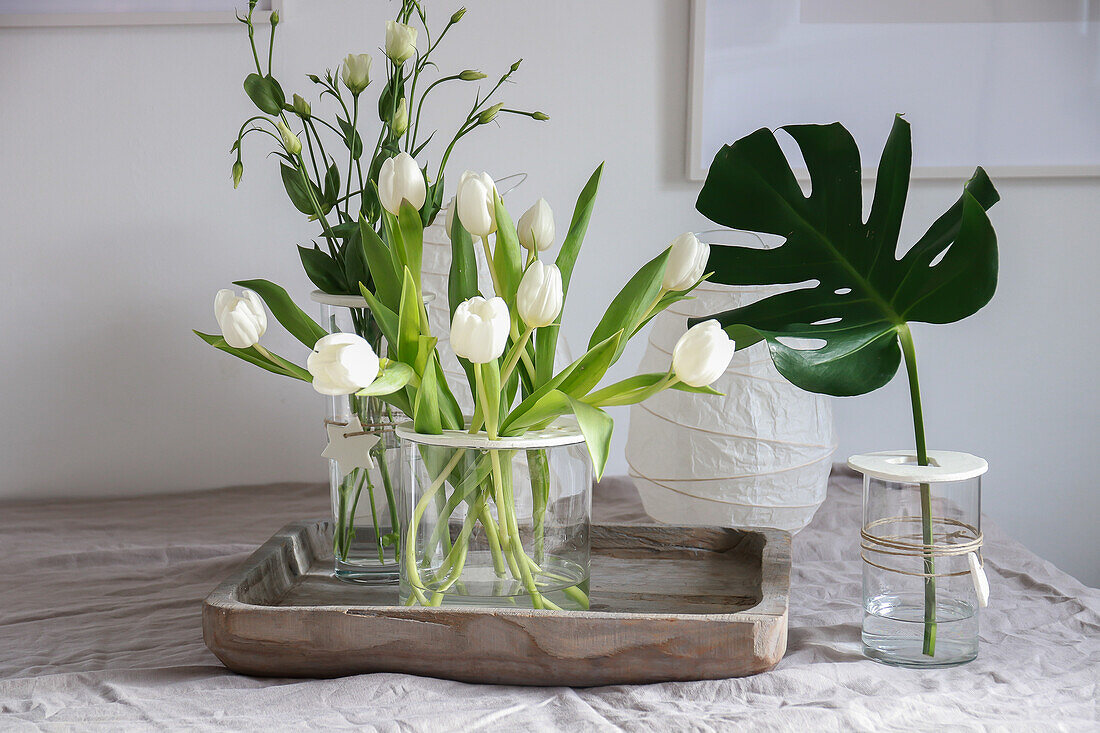 White tulips and monstera leaf in vases with homemade lid