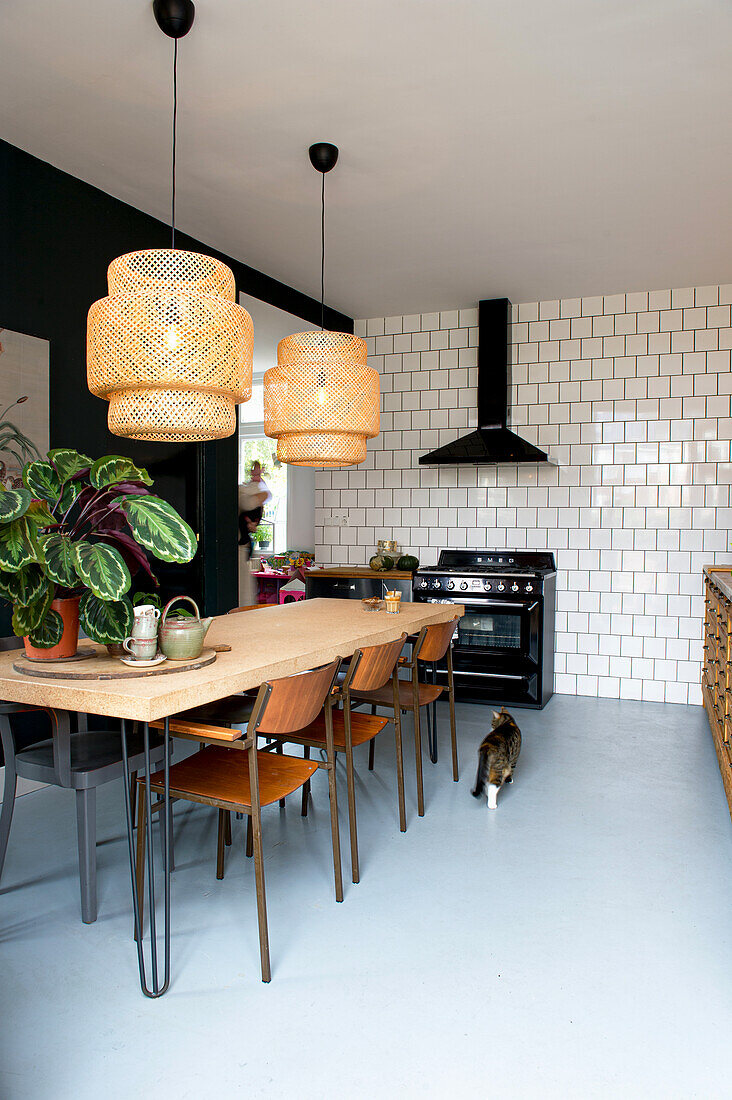 Kitchen with wooden table, retro chairs, rattan pendant lights, white tiles and cat