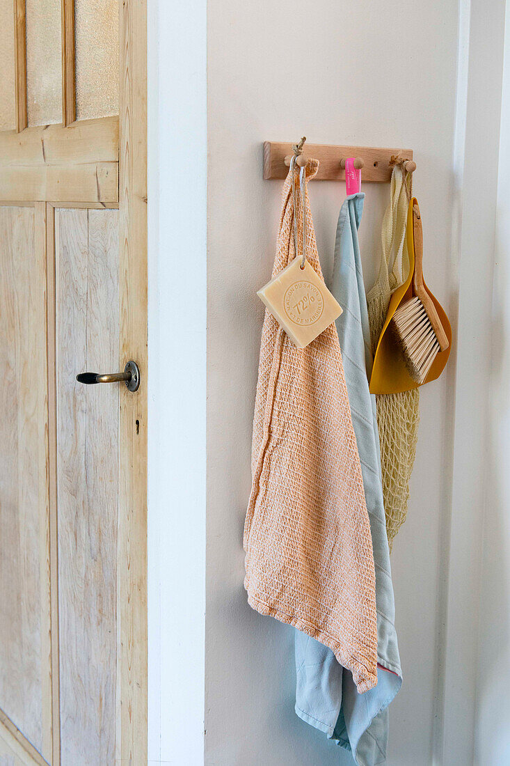 Wooden hook holder with towels and cleaning utensils on a white wall