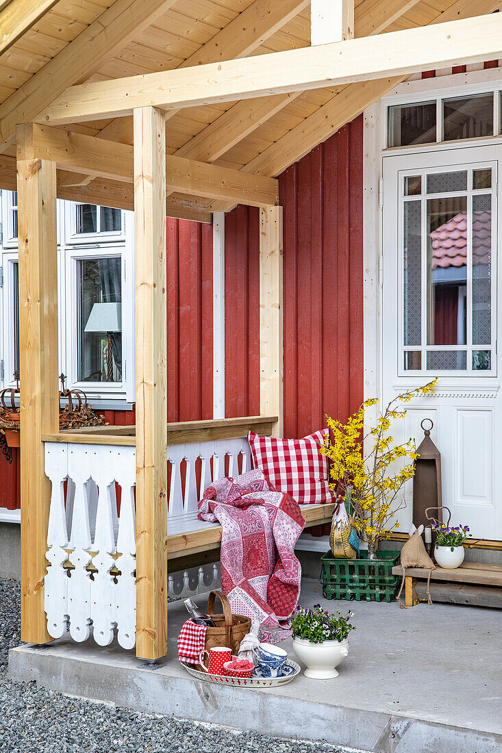 Veranda eines roten Holzhauses mit Dekorationsobjekten und Sitzgelegenheit