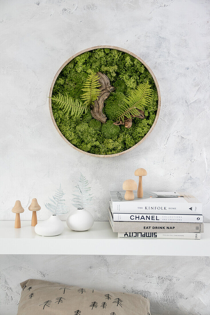 Round moss picture on a white wall above a minimalist wall shelf with decorative objects