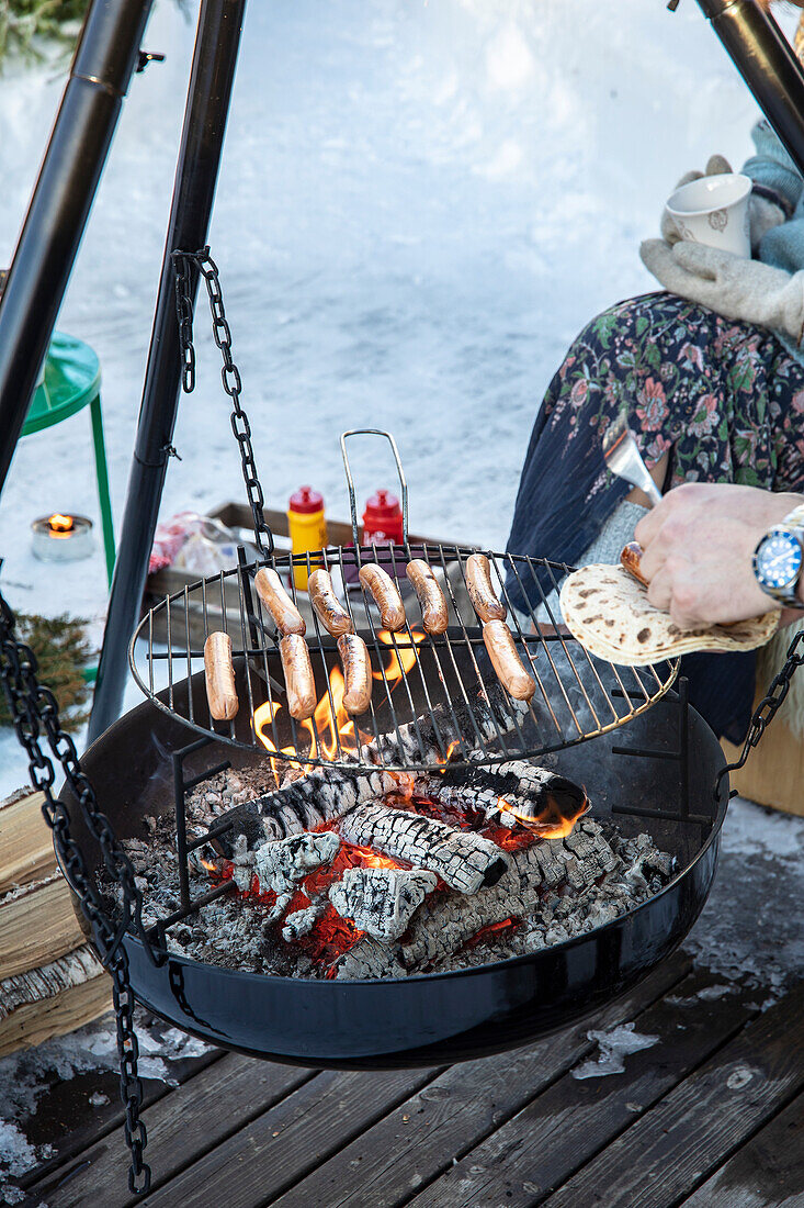 Barbecue in winter: Person roasting sausages on a swing grill