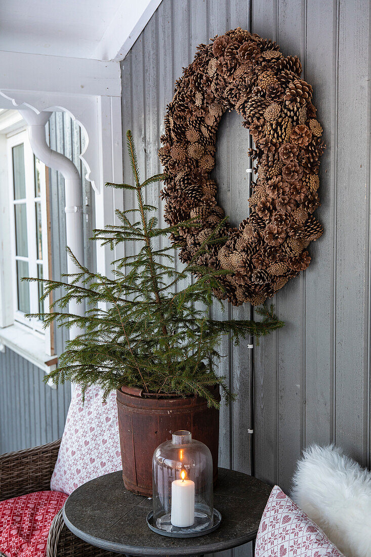 Fir cone wreath on grey wall next to Christmas tree and candle on porch