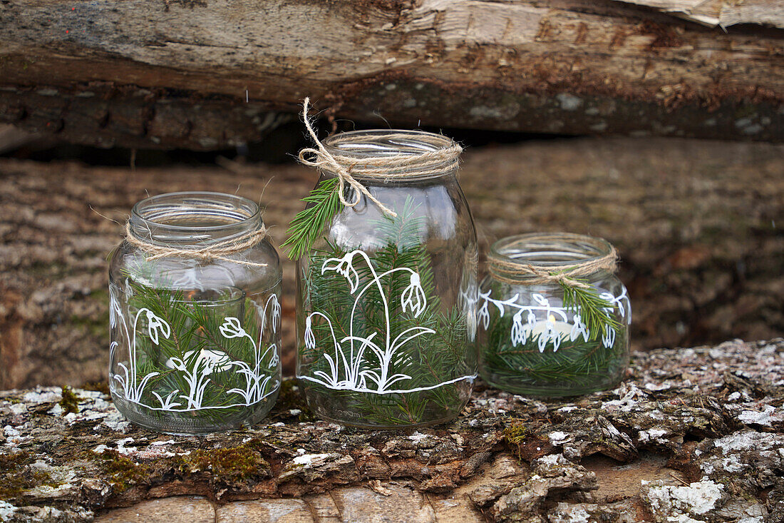 DIY Altes Glas bemalt mit Schneeglöckchenmotiv (Kreidestift)  dekoriert mit Fichtenzweigen und Schnur, Windlicht, auf einem Holzstamm