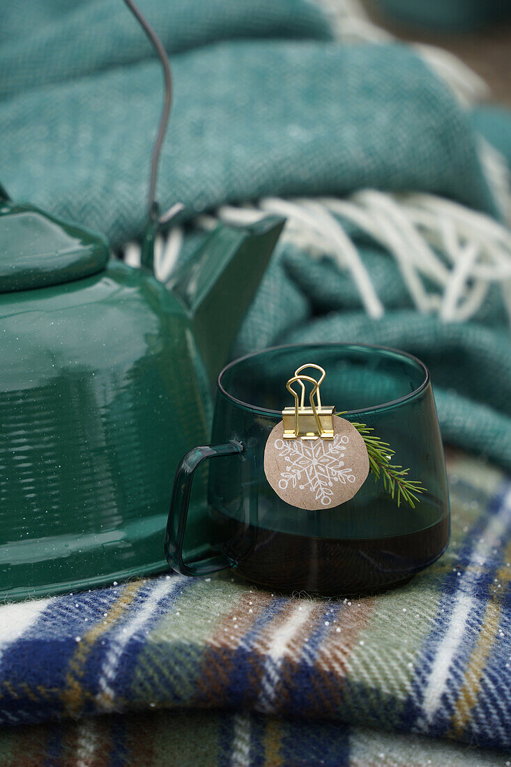 Green kettle and cup with DIY snowflake label made from wrapping paper on a checkered woolen plaid