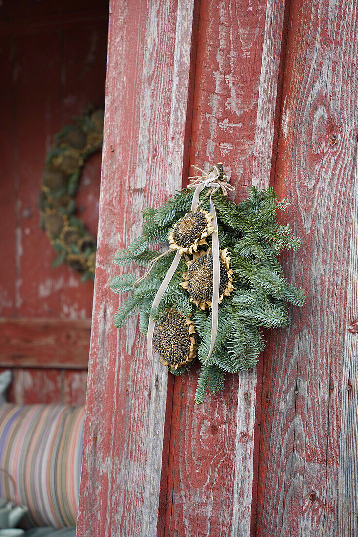 Door wreath made of fir branches and dried sunflowers on a red wooden wall