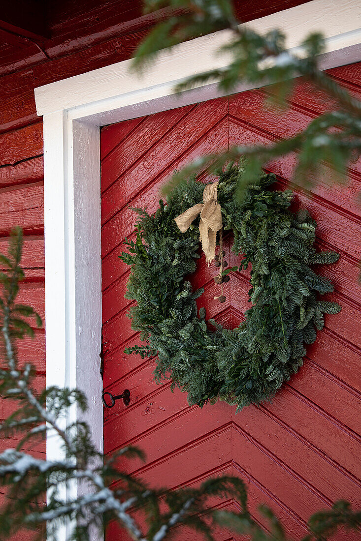 Kranz aus Tannenzweigen an roter Holztür mit weißem Rahmen