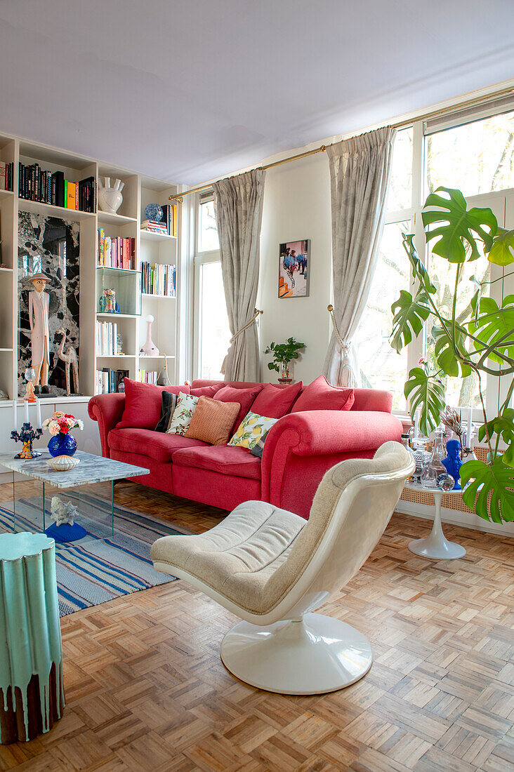 Wohnzimmer mit rotem Sofa, hellem Sessel und Bücherregal