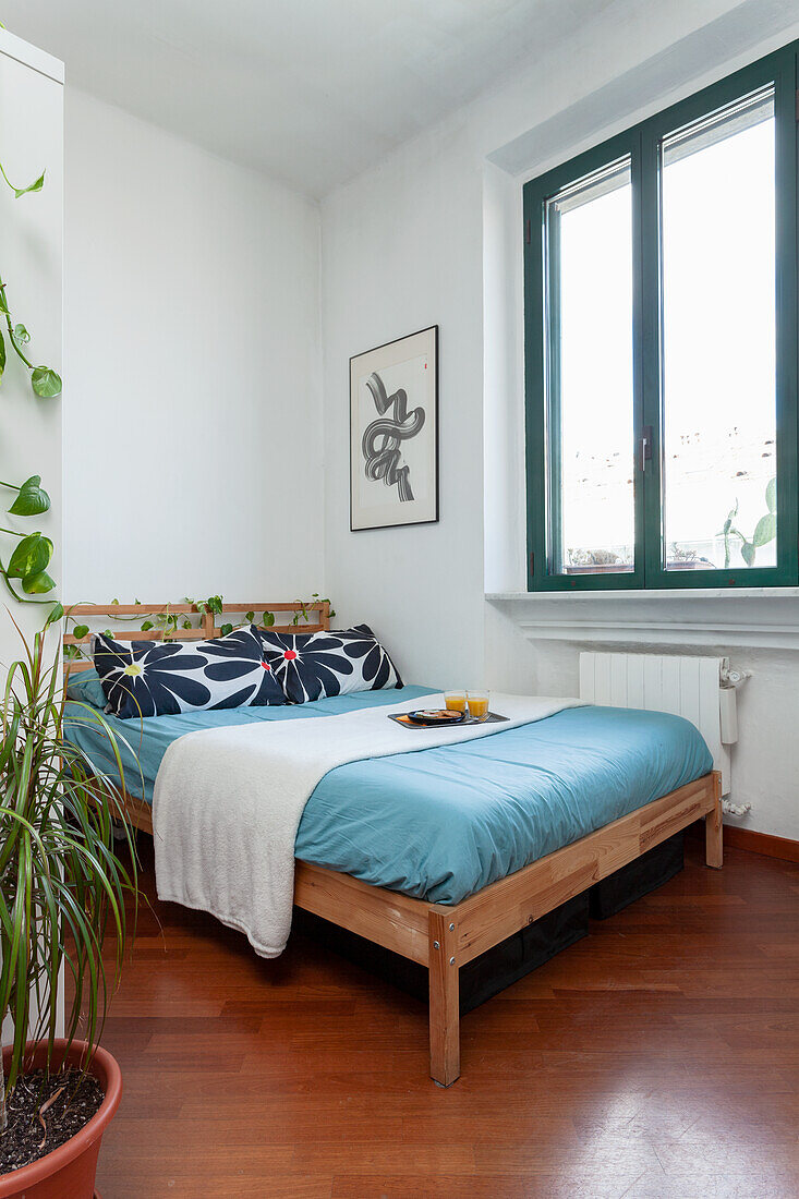 Hell möbliertes Schlafzimmer mit Pflanzen und einfachem Holzbett