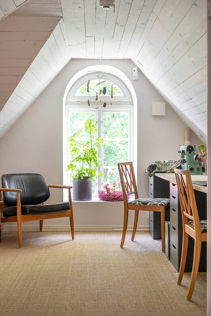 Attic room with work area, leather armchair and view of the greenery
