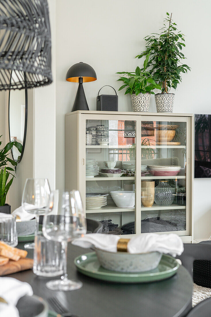 Set dining table with modern crockery and display cabinet in the background