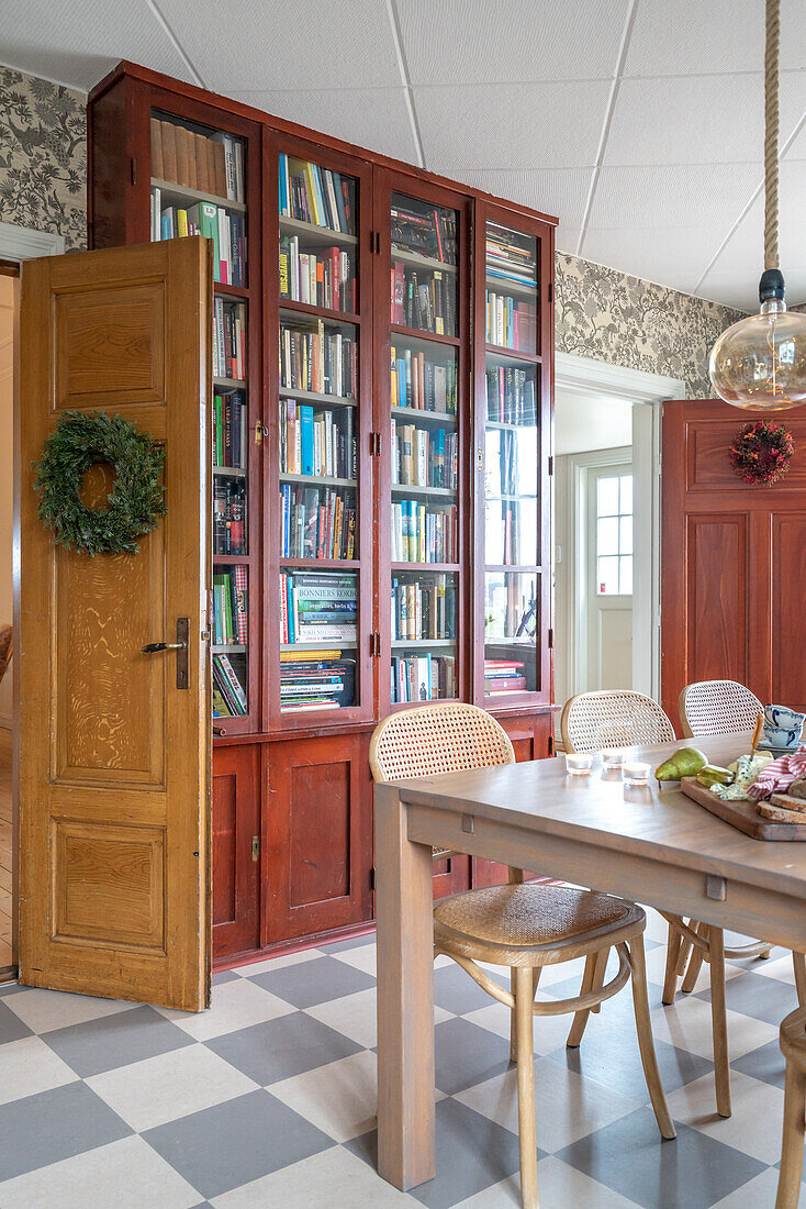 Dining table with chairs and bookcase in a room with a checkerboard pattern floor