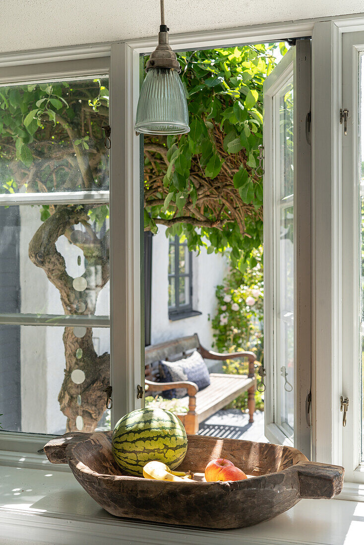 Holzschale mit Obst vor offenem Fenster, Blick auf Garten