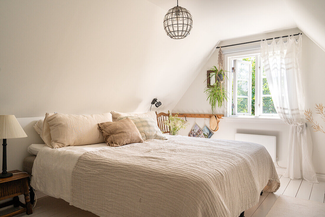 Schlafzimmer mit Dachschräge, heller Bettwäsche und Fenster mit Vorhängen