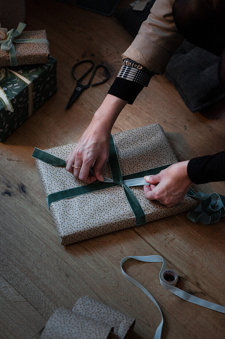 Geschenke einpacken mit gemustertem Papier und grünen Bändern auf Holzboden