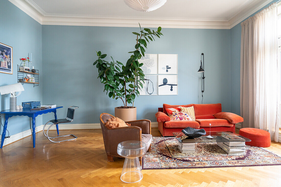 Wohnzimmer mit orangefarbenem Sofa, Leder-Sessel, hellblauen Wänden und großer Zimmerpflanze