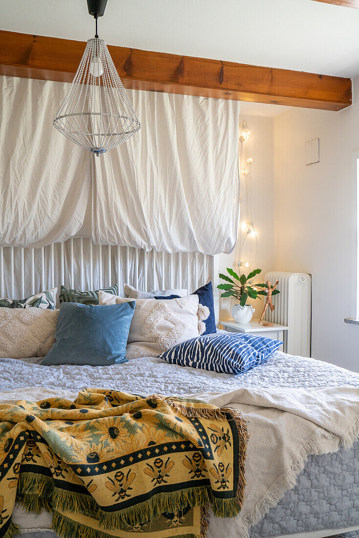 Bed with patterned and plain-coloured cushions, wire pendant light