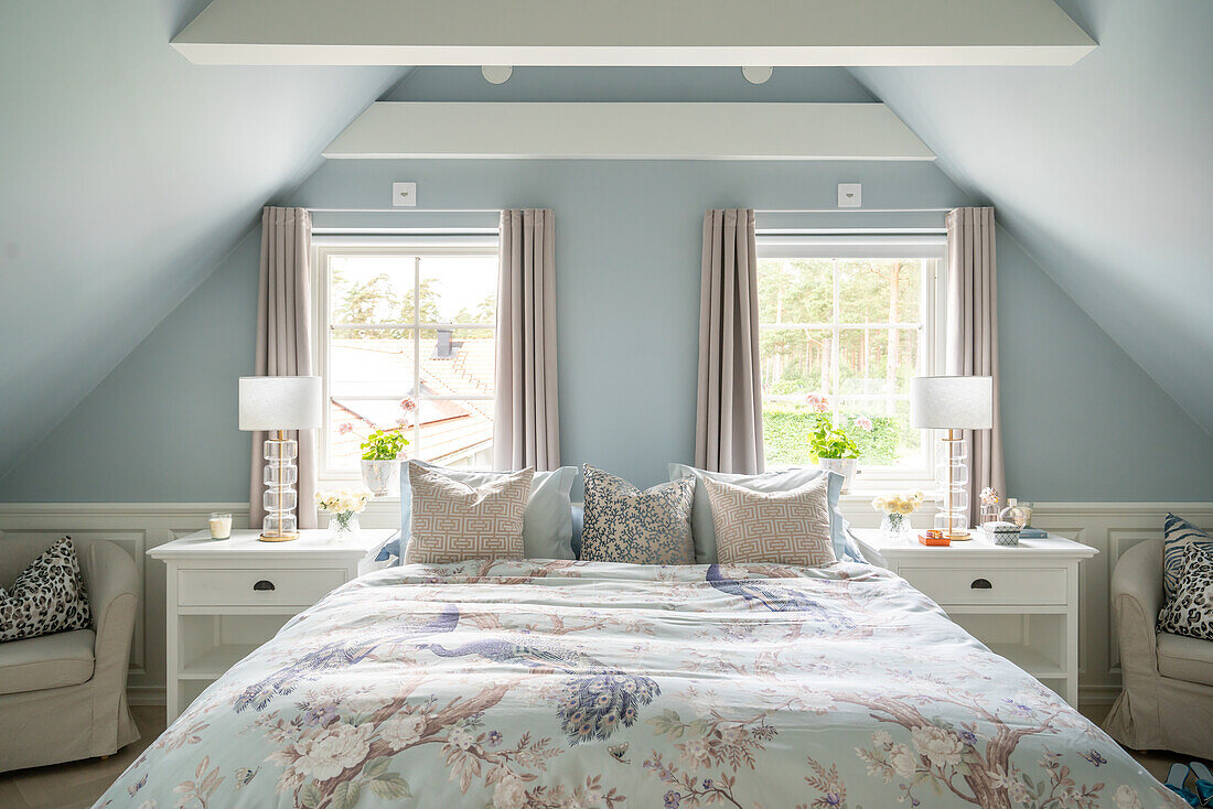 Bedroom with sloping ceilings, light blue walls and bed with floral bed linen