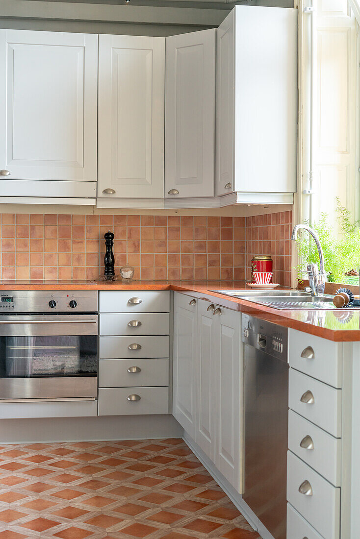 Kitchen with white cupboards, terracotta tiles on the wall and floor