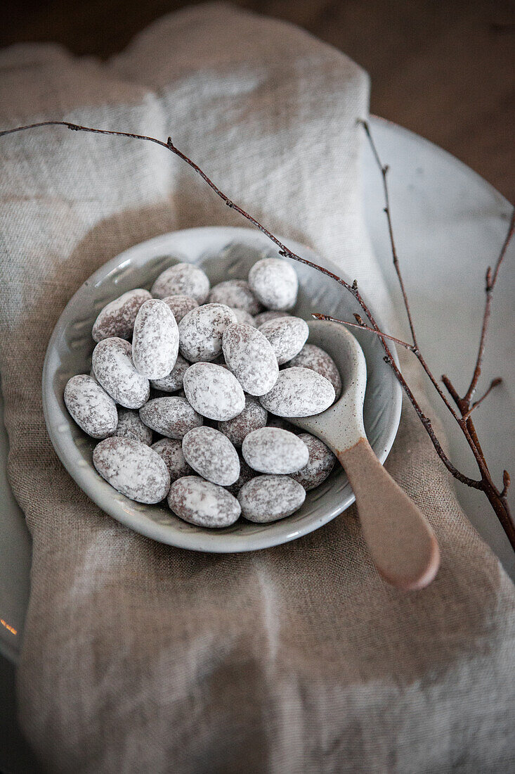 Chocolate almonds with powdered sugar in bowl on linen cloth