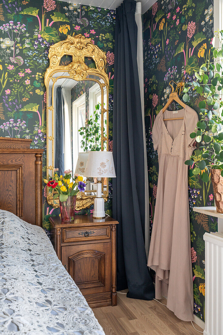 Schlafzimmer mit floraler Tapete, Holzmöbeln und Kleid an Kleiderbügel