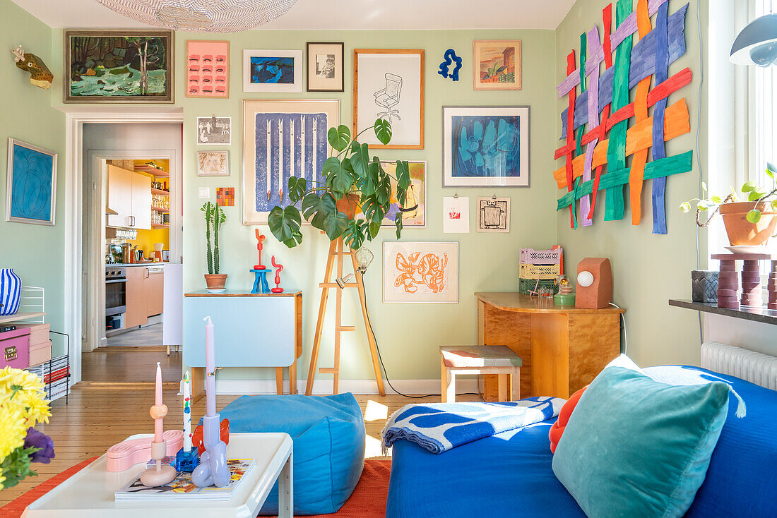 Eclectic living room with picture gallery and colorful wall hanging, blue upholstered sofa in the foreground